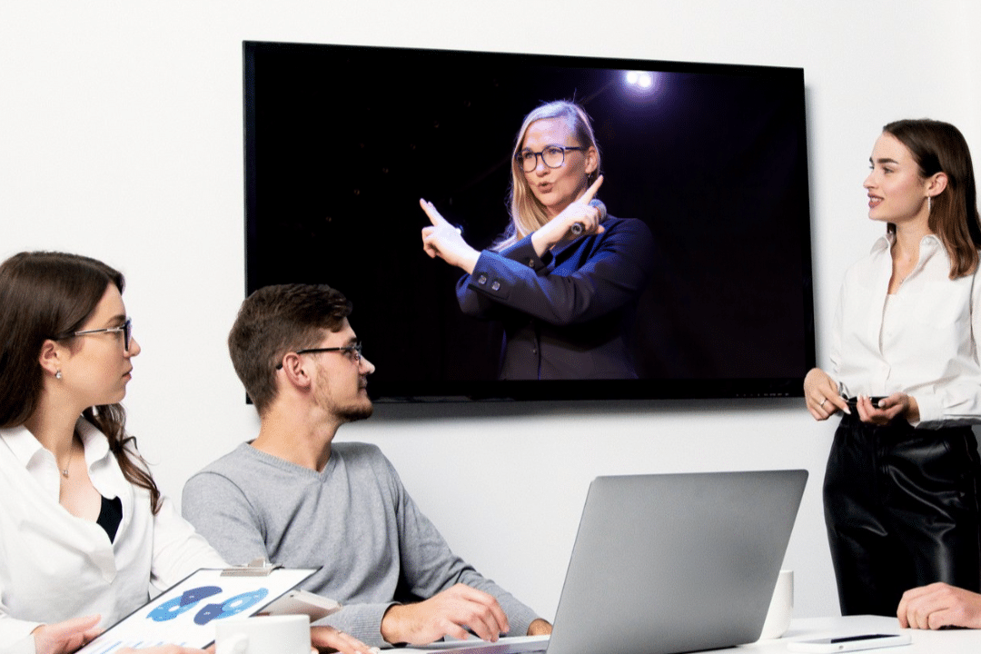 Three people in an office. They are looking at a screen showing Barbara, the founder of #VirtualSpaceHero. Relating to hybrid meetings.