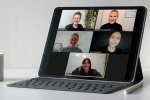 iPad showing a team meeting of 5 persons smiling into the camera.