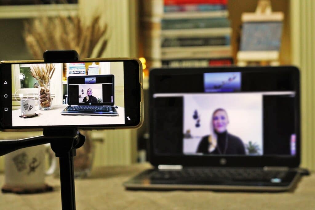 Picture Recording a virtual presentation. On the blurred laptop screen in the background you can see a woman speaking into the camera.