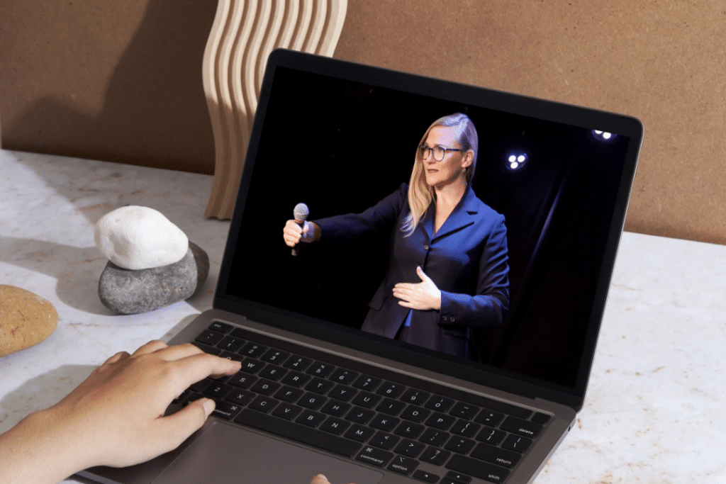 Laptop on desk showing Barbara, the founder of #VirtualSpaceHero on stage giving a speech.