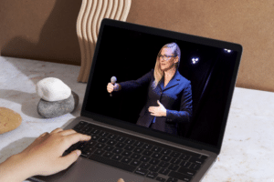 Laptop on desk showing Barbara, the founder of #VirtualSpaceHero on stage giving a speech.