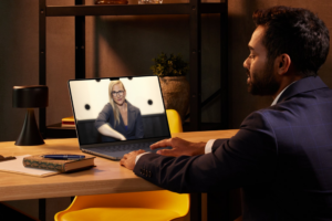 A man in a suit looking at the laptop on the desk in front of him. The screen shows Barbara, the founder of #VirtualSpaceHero, looking confident and relaxed into the camera.